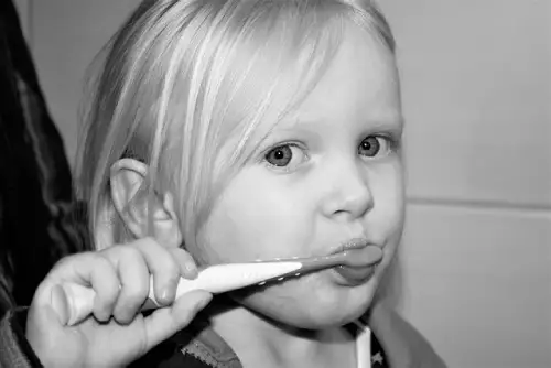 A young child brushing their teeth with a toothbrush to maintain dental hygiene and prevent teeth pain.