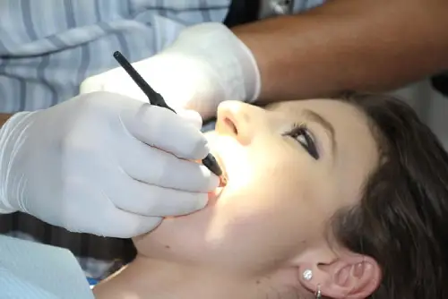 A dentist wearing white gloves uses a specialized tool to inspect the patient's teeth.