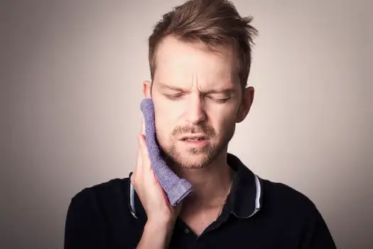 A man holding a purple warm towel to his face because he is wondering why does my jaw hurt from TMJ and stress.